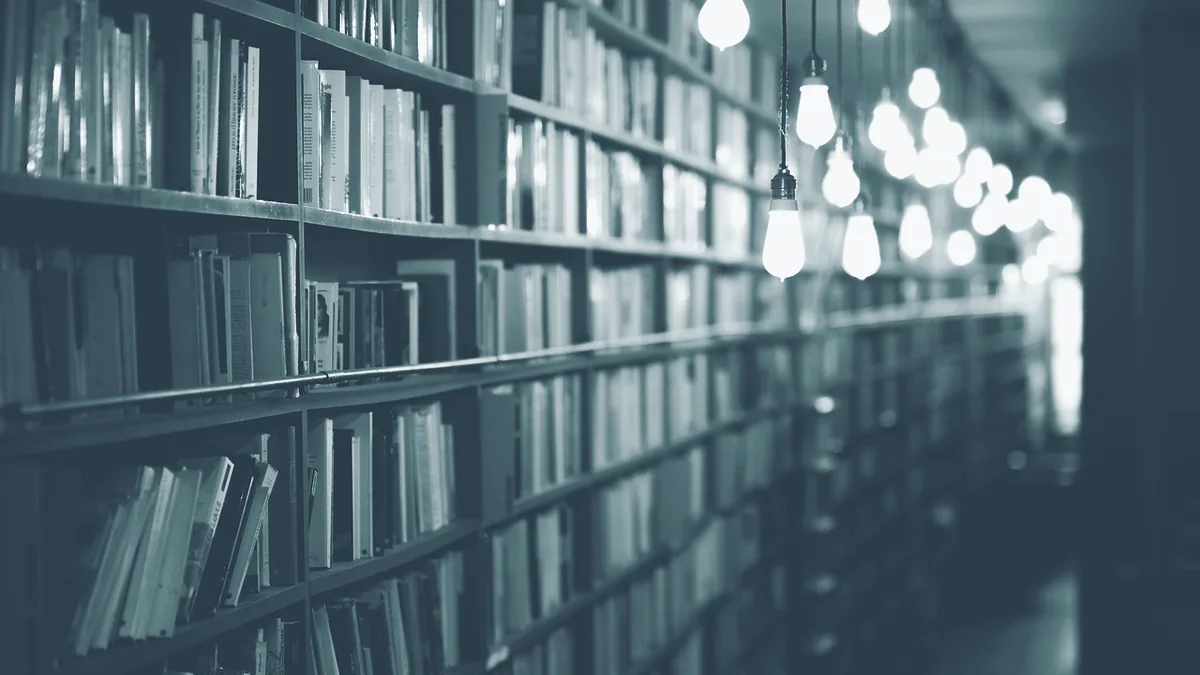 Ein langer Gang mit Regalen voller Bücher, darüber eine Reihe hängender Glühbirnen